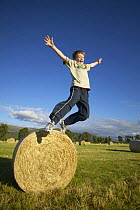Boy jumping off round hay bale, Scotland, UK