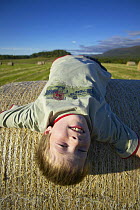 Boy lying on round hay bale, Scotland, UK Model released.