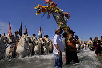 People in the sea on white horses of the Camargue. A cross and flags are carried, Saintes Maries de la mer gipsy festival, May, Camargue, France 2006