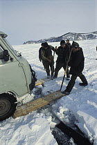 Local men preparing planks to use as bridge across cracking ice plate, a mile out from shoreline of Lake Baikal, world's deepest and oldest (and largest by volume) freshwater lake, Siberia, Russia BB...