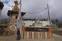 Old lady next to prayermill with Chorten of Geling in background, Nepal