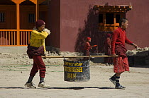 Young buddhist monks using pole to carry metal rubbish bin, Chhode Gompa, Lo-Manthang, Upper Mustang, Nepal
