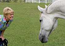 Woman face to face with grey Trakhener gelding, in field, Longmont, Colorado, USA. Model released.