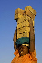Woman carrying bricks made by digging up surrounding soil, individually moulding the bricks, building kilns and using large quantities of fire wood. Madagascar  2005