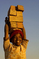 Child carrying bricks made by digging up surrounding soil, individually moulding the bricks, building kilns and using large quantities of fire wood. Madagascar