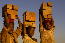 Children carrying bricks made by digging up surrounding soil, individually moulding the bricks, building kilns and using large quantities of fire wood. Madagascar