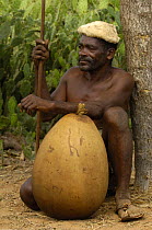 Antandroy herdsman wearing hat made from goat skin and shoes from Zebu skin. The gourd is for storing water or milk and the top is closed off with a corn cob. Spiny forest of Southern MADAGASCAR.  200...