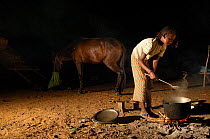 Fulani woman cooking at night, horse in background, North Senegal, West Africa, 2005