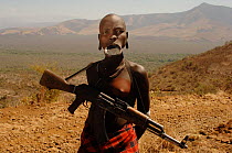 Young Mursi woman with clay plate in lower lip, holding her Kalashnikov rifle (result of the cold war in Africa), Omo valley, Ethiopia, 2006