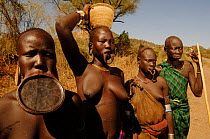 Group of Mursi women with and without their clay plate in lower lip, with other members of the tribe behind, Omo valley, Ethiopia, 2006
