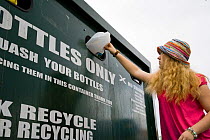Woman putting plastic bottle into recycling bin in supermarket carpark, Shrewsbury, Shropshire, UK 2007, model released