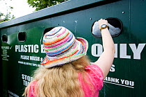 Woman putting plastic bottle into recycling bin in supermarket carpark, Shrewsbury, Shropshire, UK, 2007. Model released