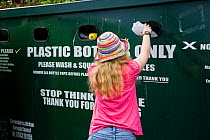 Woman putting plastic bottle into recycling bin in supermarket carpark, Shrewsbury, Shropshire, UK, 2007. Model released