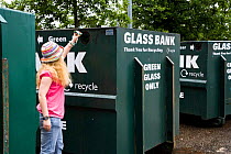 Woman putting glass bottle into recycling unit in supermarket carpark, Shrewsbury, Shropshire, UK, 2007 model released