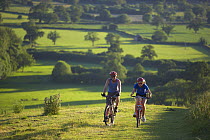 Man and woman on mountain bikes cycling on Hambledon Hill above the Blackmore Vale, Dorset, England, UK