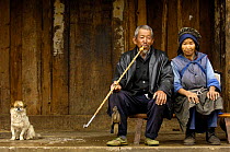 Naxi woman with man smoking a long-stemmed bamboo pipe with a dog at his side, Lijiang Yunnan Province, China 2006