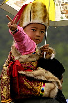 Child in traditional dress making V sign at the Horse Racing Festival or 'Heavenly Steed Festival' which takes place on the 5th and 6th days of the fifth lunar month. Zhongdian, Deqin Tibetan Autonymo...