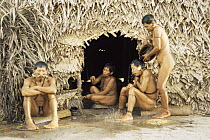 Matis Indian people in daily life routines, sitting in home huts and washing, Amazonia, Brazil.  Facial decorations are thought to mimic jaguars.