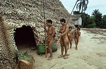 Matis Indians men and boys gather outside traditional home hut, Amazonia, Brazil. Note jaguar skin drying