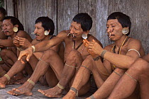 Matis Indians sitting outside hut, Amazonia, Brazil.  Facial decorations mimic jaguar markings.