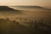 View along the limestone Cotswold escarpment and misty countryside at dusk, Coaley Peak, Gloucestershire, England