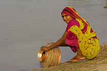 Rabari woman washing brass water pot in the salt pans. Rann of Kutch, Gujarat, SW India
