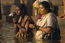 Two women praying in the River Ganges, Varanasi, Uttar Pradesh, India. Feb 2007