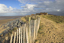 Chestnut fencing and granite boulders protecting coastal dunes and buildings, Norfolk, UK