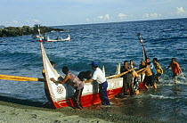 Tao tribe crew push ten-man hand-made traditional plankboat or Cinedkeran ashore, Orchid Island, Taiwan. Small tatala plank boat in background. 2007