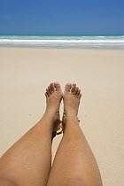 Woman's bare legs and feet on white sand, Broome's Cable Beach, Western Australia