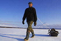 Photographer Igor Shpilenok pulling equipment in sledge with Kronotsky Volcano, Kamchatka, Russia
