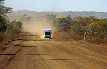 Dust cloud following a Camper van driving along unpaved road in Karijini National Park, Western Australia