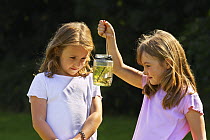 Two girls studying fish in a jar, Northamptonshire, England, July 2007