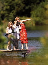 Family - woman and two girls - beside lake enjoying the outdoors, watching birds with binoculars and pond dipping with net,   Northamptonshire, July 2007
