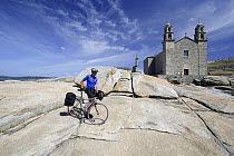 Cyclist on the granite rocks outside the Church of our Lady of the Boats, on the coast of Muxia, Costa da Morte, Galicia, Spain