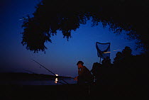 Fisherman at night on lake side, with star trails in background, Hungary.
