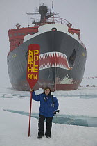Photographer Sue Flood standing next to North Pole sign surrounded by water, on a tourist trip to the North Pole July 2007