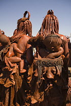 Two women of the Himba tribe, Kaokoland, wearing distinctive headdress and clothing, with children strapped to their backs. Namibia