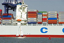 Container ship at dockyard with small sailing craft in foreground, Felixstowe, Suffolk, England, UK