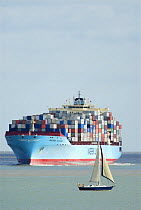Container ship approaching Felixstowe docks with small sailing craft in foreground, Suffolk, England, UK