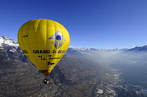Hot air balloon in flight over the Aosta Valley, northern Italian Alps, with early morning mist / temperature inversion
