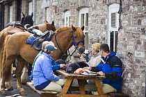 Horses and riders relaxing outside the Three Horseshoes Pub on a horse-riding trekking holiday, Brecon Beacons National Park, Powys, Wales, UK, Model released