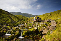 Walkers resting beside stream,  Llyn y Fan Fach, Brecon Beacons National Park, Powys, Wales