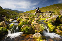 Walkers relaxing beside moorland stream, reading map at Llyn y Fan Fach, Brecon Beacons National Park, Powys, Wales