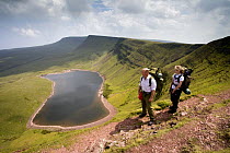 Walkers carrying backpacks above Llyn y Fan Fach, a glacial cirque, beneath Black Mountain in the Brecon Beacons National Park, Powys, Wales