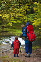 Adult walker carrying child in backpack with another child walking, in waterfall country along the Nedd Fechan, Brecon Beacons National Park, Powys, Wales