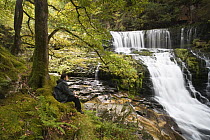 Walker relaxing beside Clyn-Gwyn waterfalls, Brecon Beacons National Park, Powys, Wales