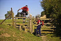 Walkers crossing a wooden stile on a public footpath, Bledington, Oxfordshire, UK