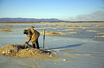 A fisherman from the Hezhe ethnic minority fishes through holes in the ice on the Black Dragon River, Heilongjiang Province, north-east China. January 2007