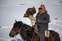 A Kazakh hunter riding horse with his Golden eagle, out hunting in the Altai mountains of Xinjiang Province, north-west China. February 2007